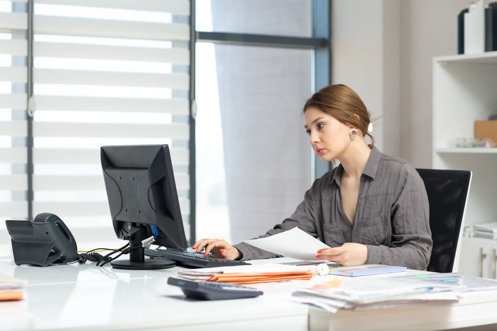 Mitarbeiterin im Innendienst arbeitet am Bildschirm mit Unterlagen auf dem Tisch