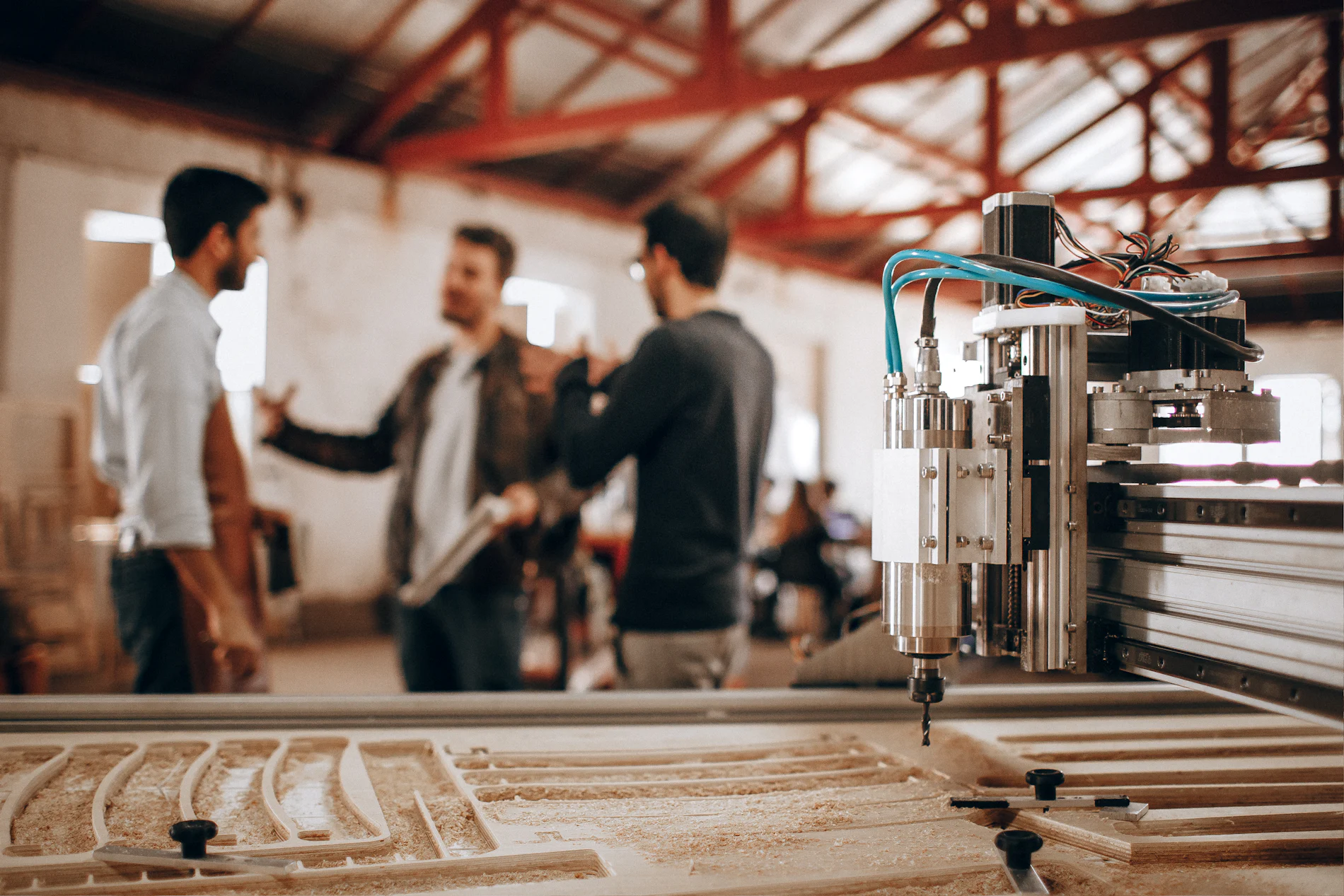Drei Kollegen besprechen sich in einer Fertigungshalle neben einer CNC-Maschine